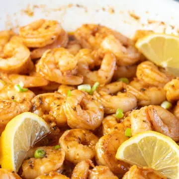 Wide image of new orleans bbq shrimp in pan with lemon slices.