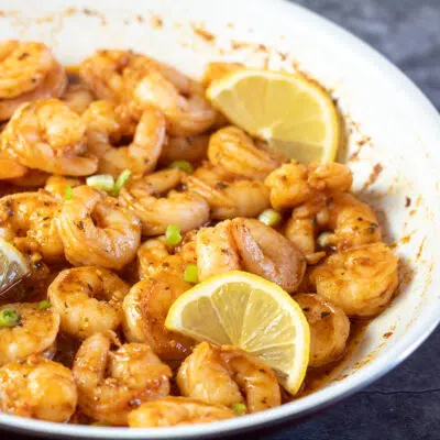 Square image of new orleans bbq shrimp in pan with lemon slices.