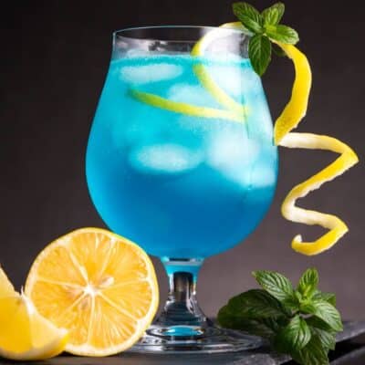 Best blue lagoon cocktail drink recipe is served with lemon twist and basil garnish.