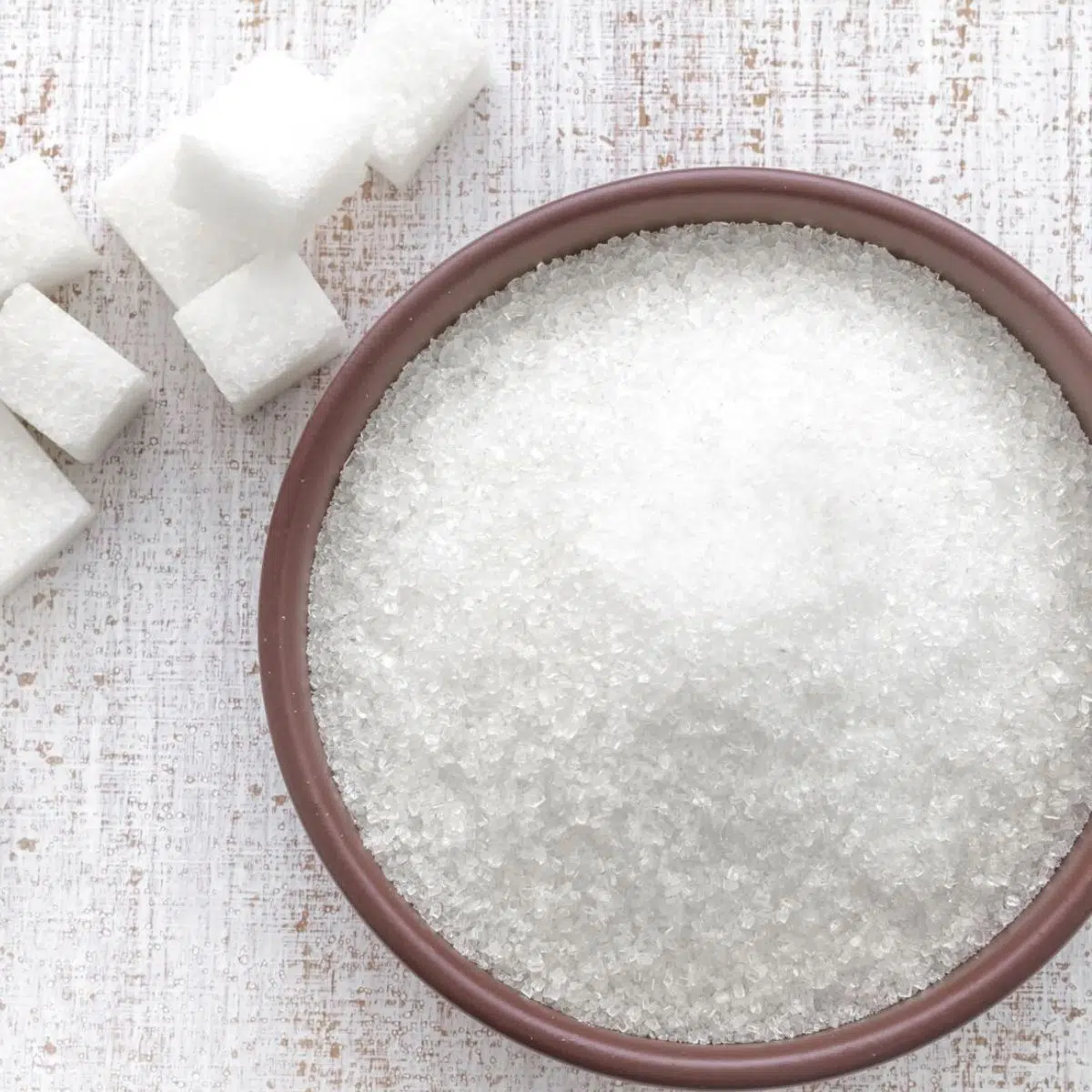 Grams of sugar to cups conversion guide featuring sugar in a bowl with sugar cubes beside it.