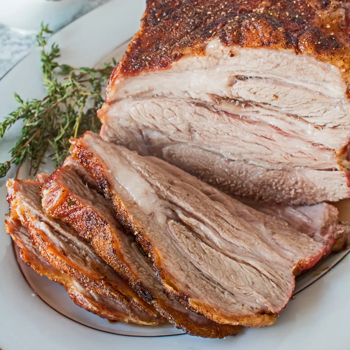 Квадратно изображение на свинска плешка, печена върху чиния за сервиране, нарязана на резени.