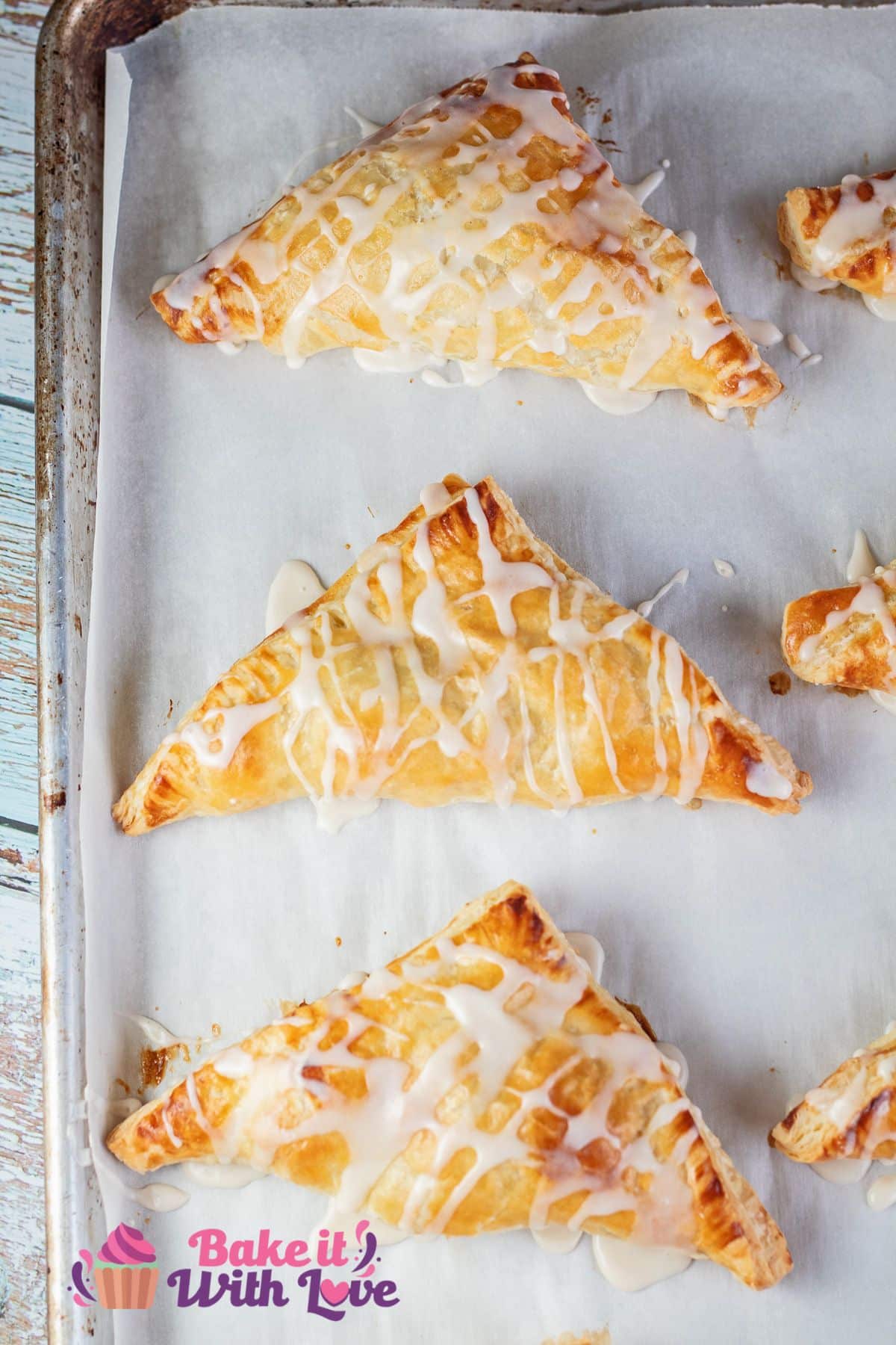 Easy puff pastry apple turnovers on baking sheet after adding vanilla icing drizzle.