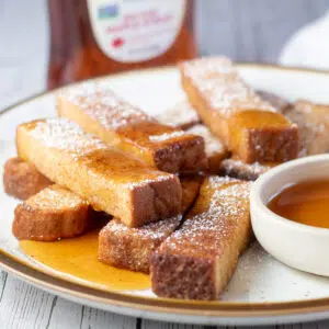 Square image showing air fryer french toast sticks on a plate with maple syrup.