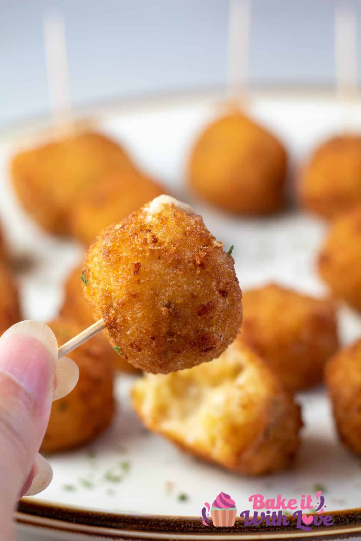 Tall image of air fryer mac & cheese bites on a plate, with one being held up by a toothpick.