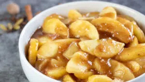 Wide image of apple pie filling in a white bowl.