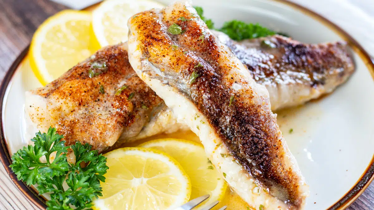 Wide image of baked monkfish on a plate with lemon slices.