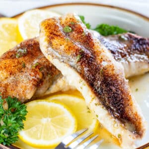 Close up square image of baked monkfish on a plate with lemon slices.