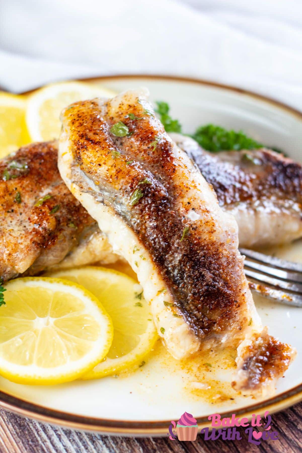 Tall image of baked monkfish on a plate with lemon slices.