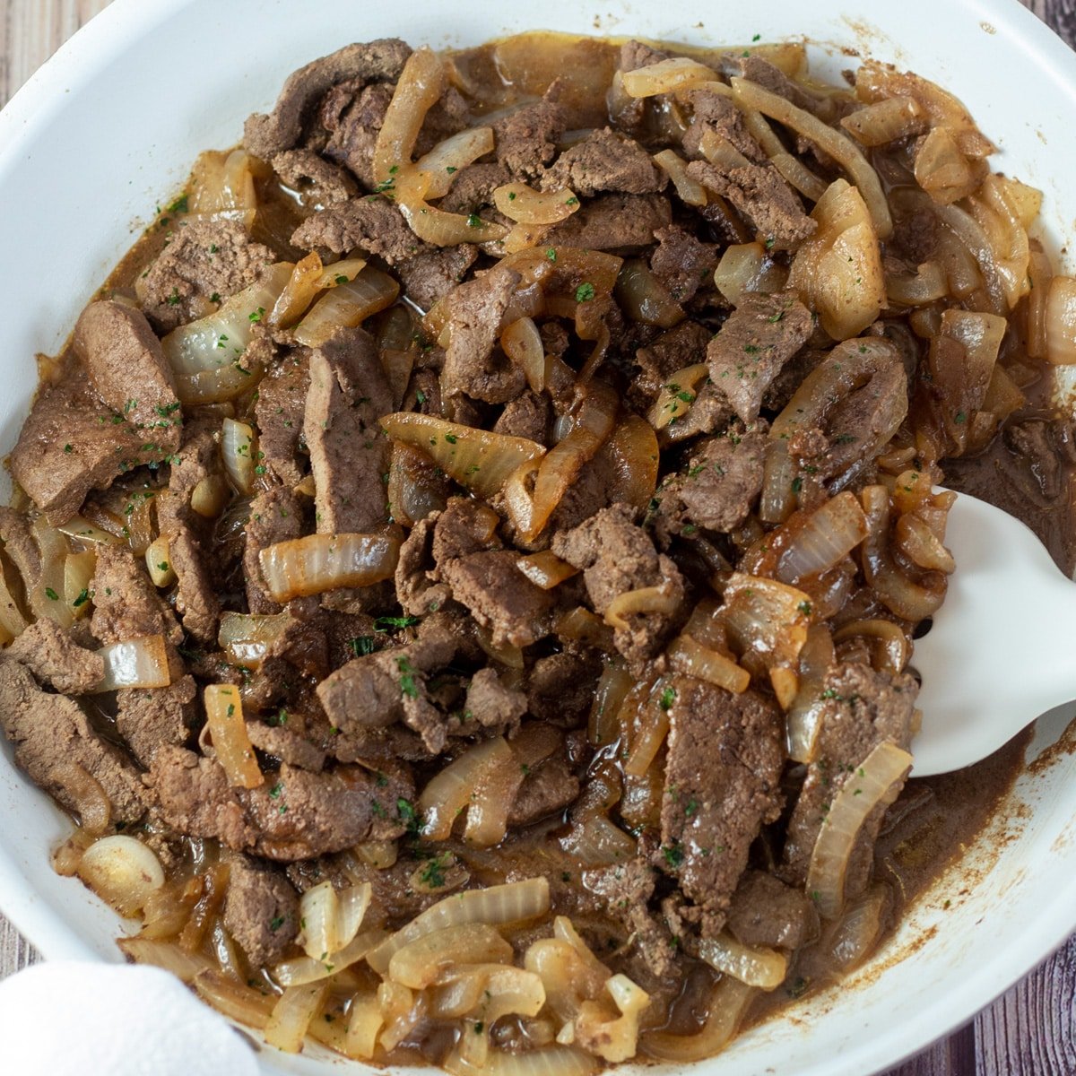 Square image of beef liver and onions in a frying pan.