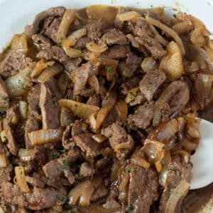 Closeup square image of beef liver and onions in a frying pan.