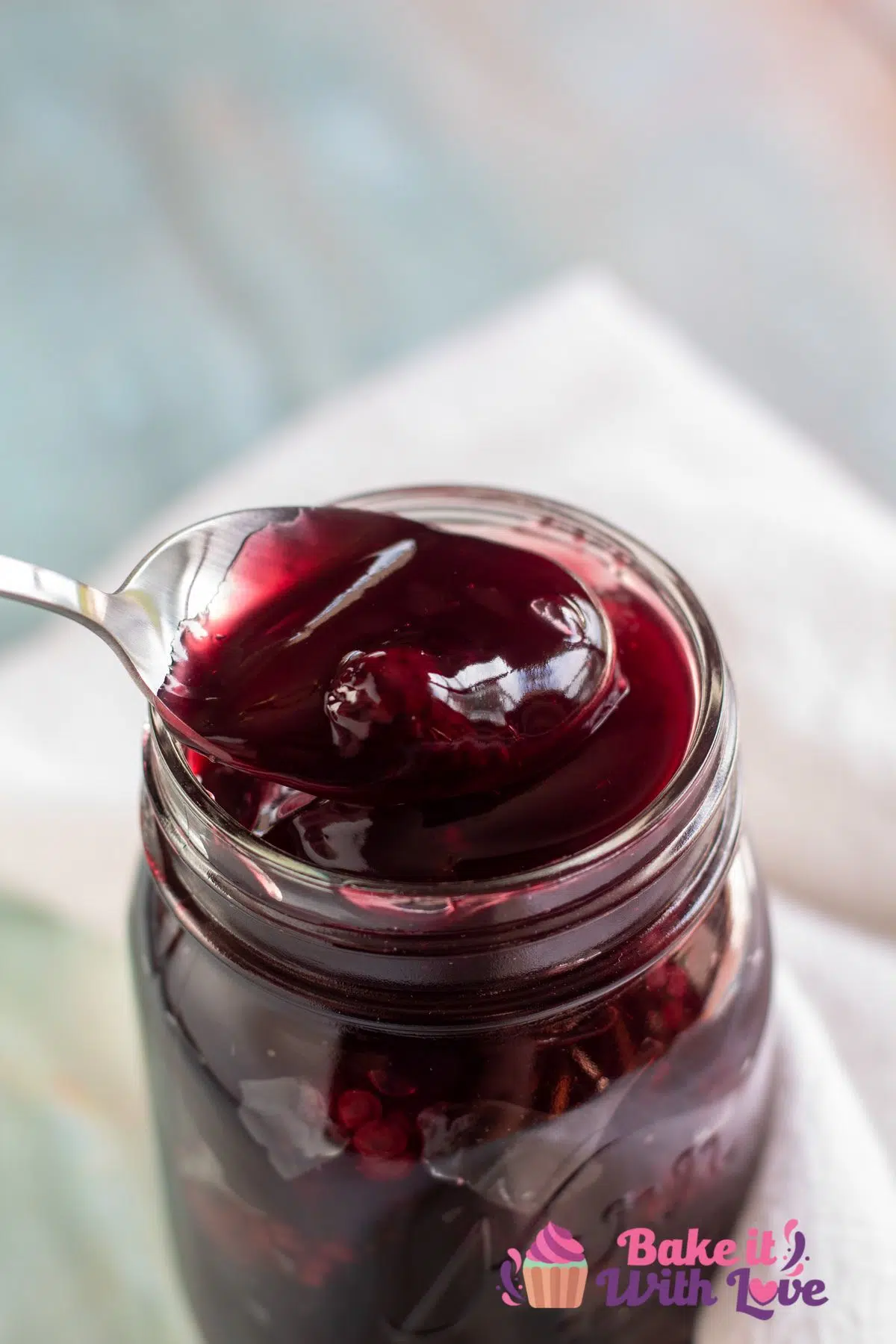 Tall image of blackberry pie filling in a glass jar with a spoon full of the pie filling.