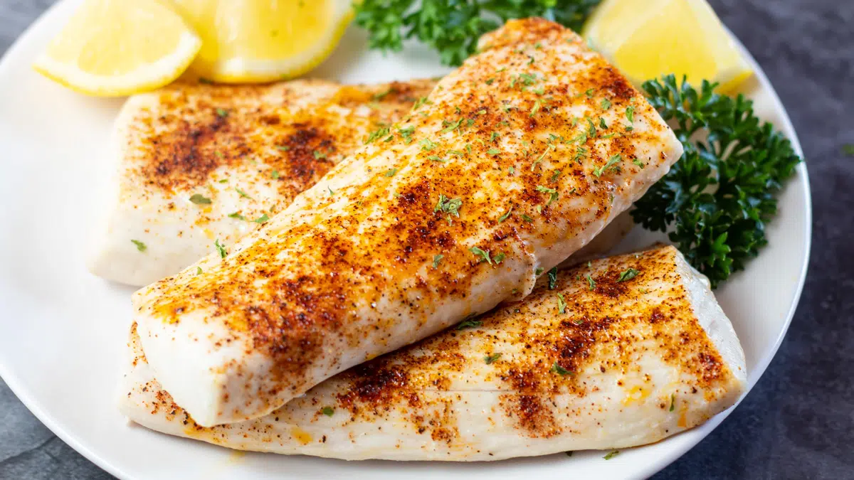 Wide image showing broiled mahi mahi filets on a white plate.