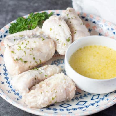 Square image of butter poached monkfish on a plate with a small bowl of drawn butter to dip in.