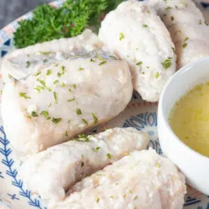 Close up square image of butter poached monkfish on a plate with a small bowl of drawn butter to dip in.