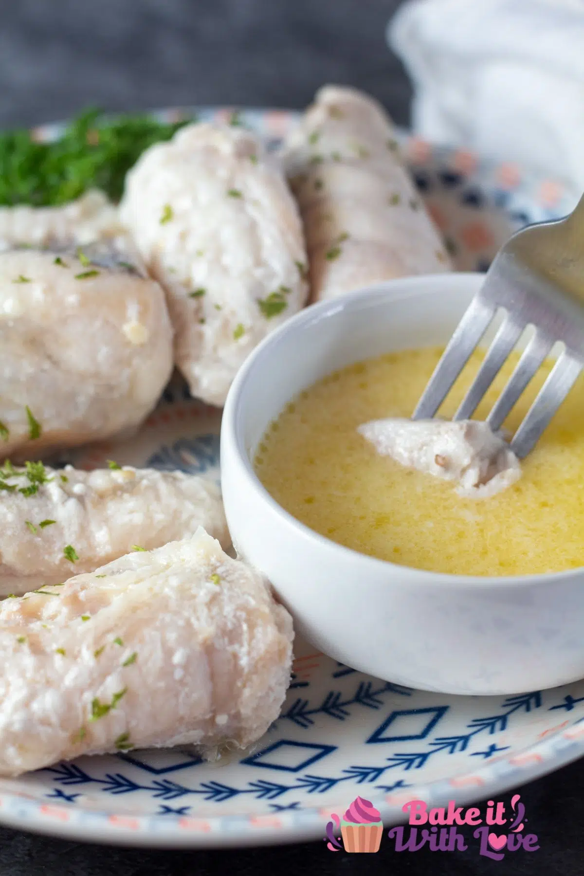 Tall image of butter poached monkfish on a plate, dipping a piece of monkfish into drawn butter.