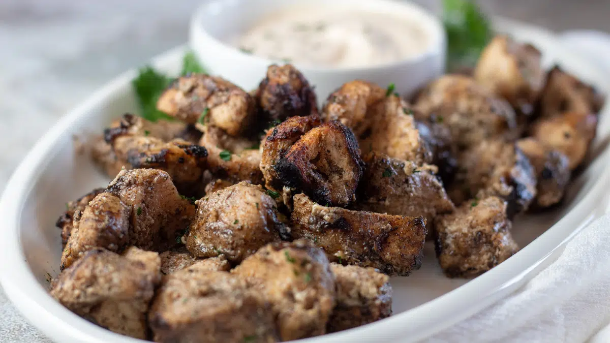 Wide image of Cajun alligator bites on a white serving plate with dipping sauce.