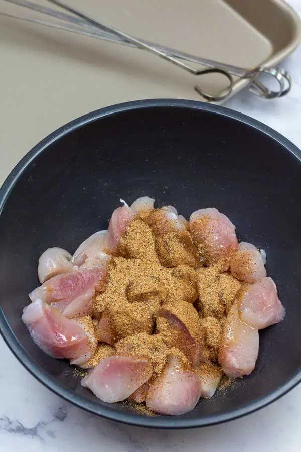 Process image 1 showing cut up alligator meat in a bowl with Cajun seasoning.
