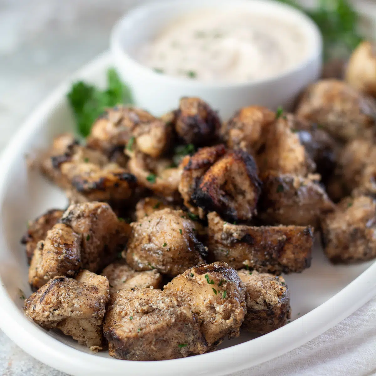 Square image of Cajun alligator bites on a white serving plate with dipping sauce.