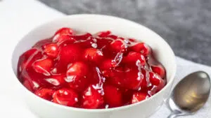Wide shot image of cherry pie filling in a white bowl.