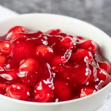 Wide shot image of cherry pie filling in a white bowl.