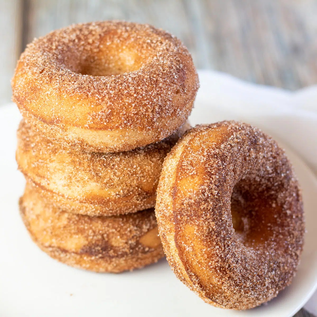 Imagem quadrada de donuts assados ​​com açúcar de canela empilhados em um prato branco.