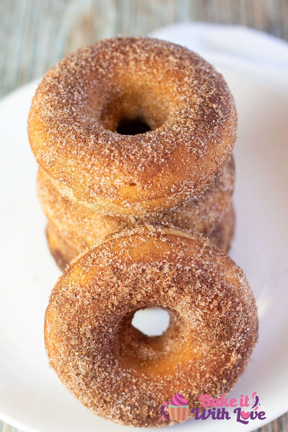 Tall image of cinnamon sugar baked donuts stacked on a white plate.