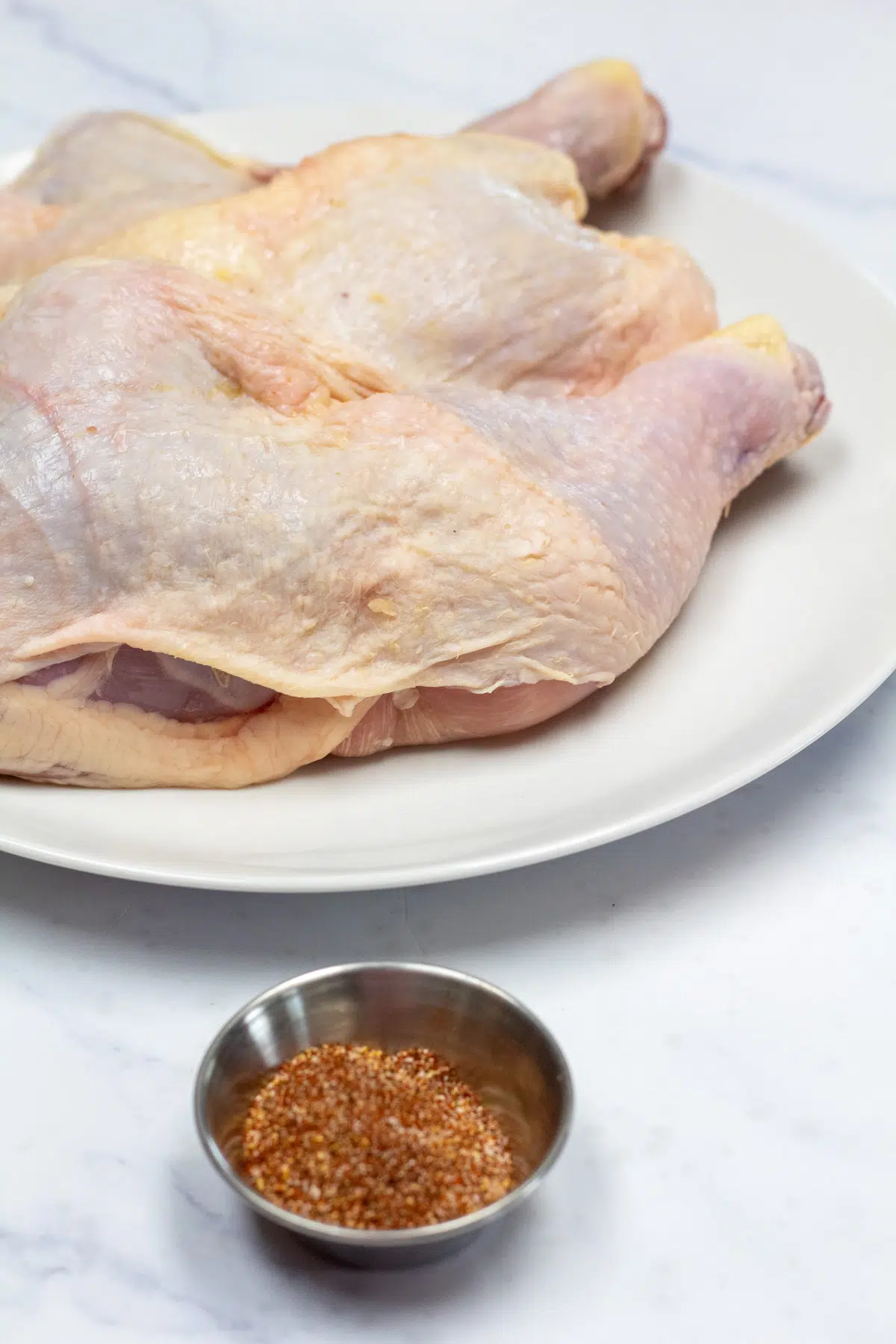 Tall photo showing chicken leg quarters and seasoning.