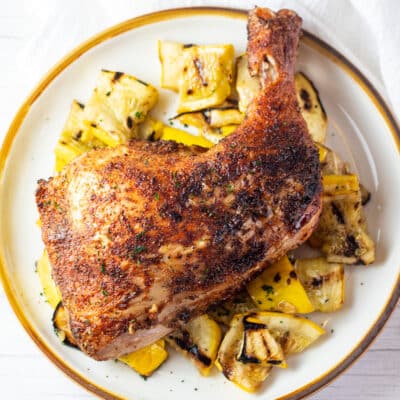 Square image of grilled chicken leg quarters over sauteed yellow squash.