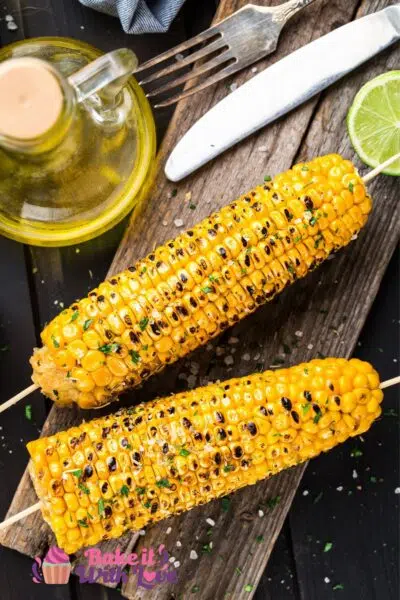 Tall image of grilled corn on the cob with wooden skewers.