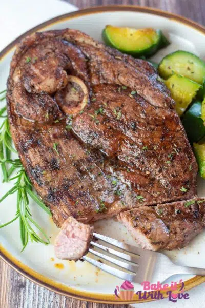 Tall image of grilled lamb steak on a plate with zucchini and rosemary.