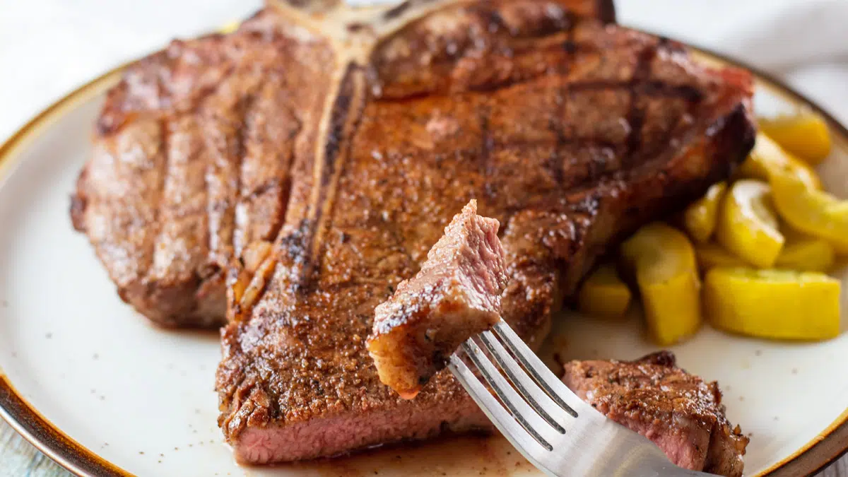 Wide image of a grilled t bone steak on a plate.
