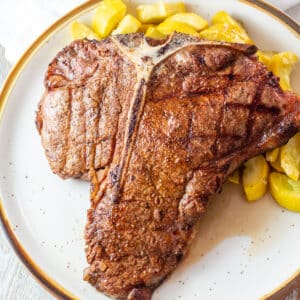 Square image of a grilled t bone steak on a plate.