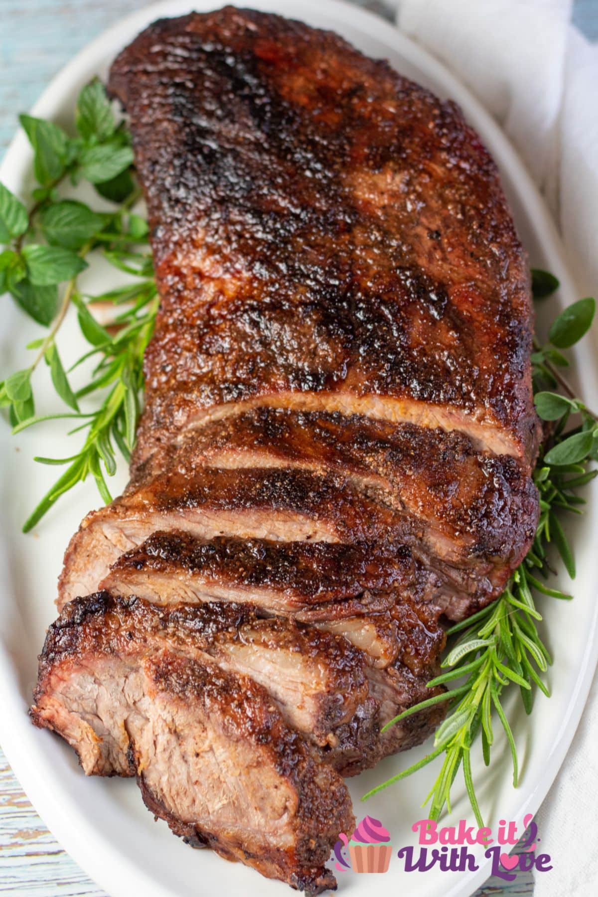 Tall overhead image of sliced grilled beef tri-tip on a white serving platter.