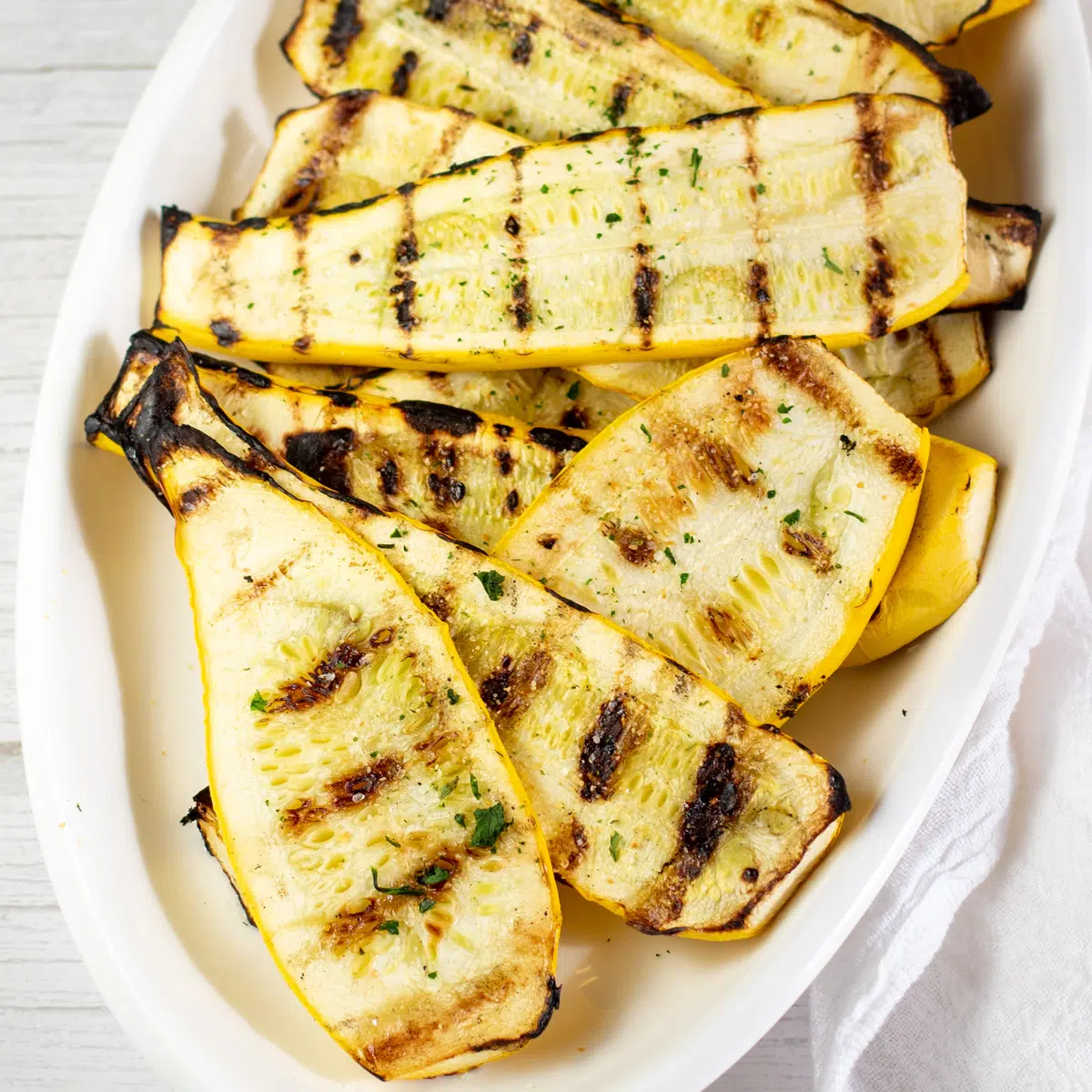 Square image of grilled yellow squash on a white serving plate.
