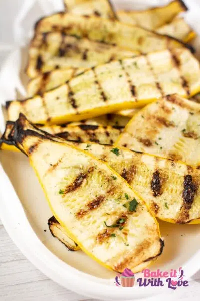 Tall image of grilled yellow squash on a white serving plate.