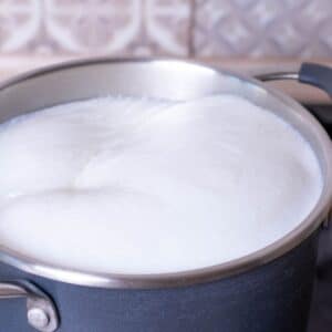 Homemade sweetened condensed milk in saucepan cooking until thickened.