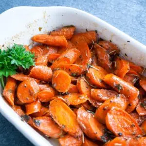 Square image of roasted honey glazed carrots in a white baking dish.
