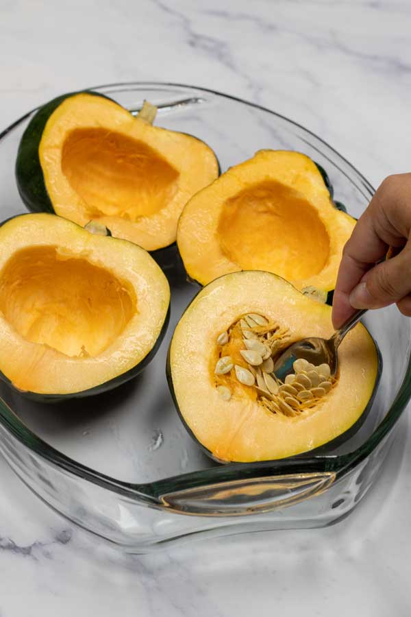 Process image 2 showing acorn squash cut in half in a baking dish scooping seeds out.