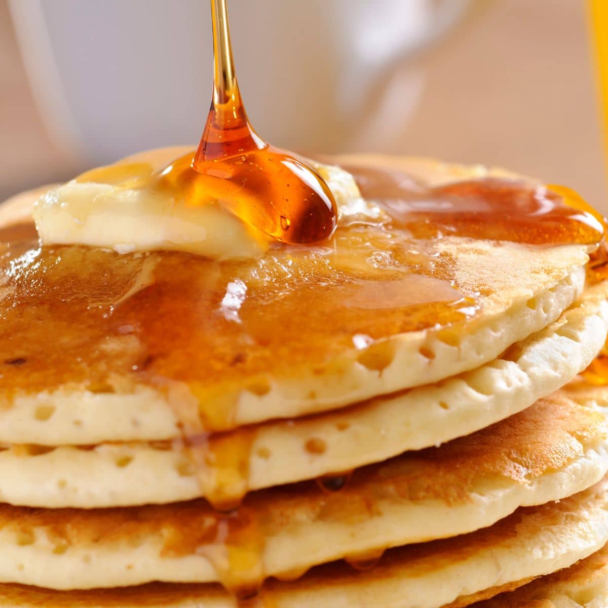 Square image of pancakes with syrup being poured over them.