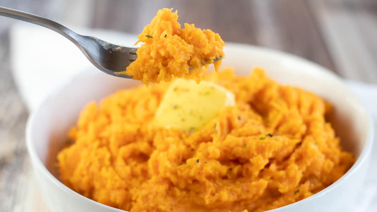 Wide image of mashed sweet potatoes in a white bowl.