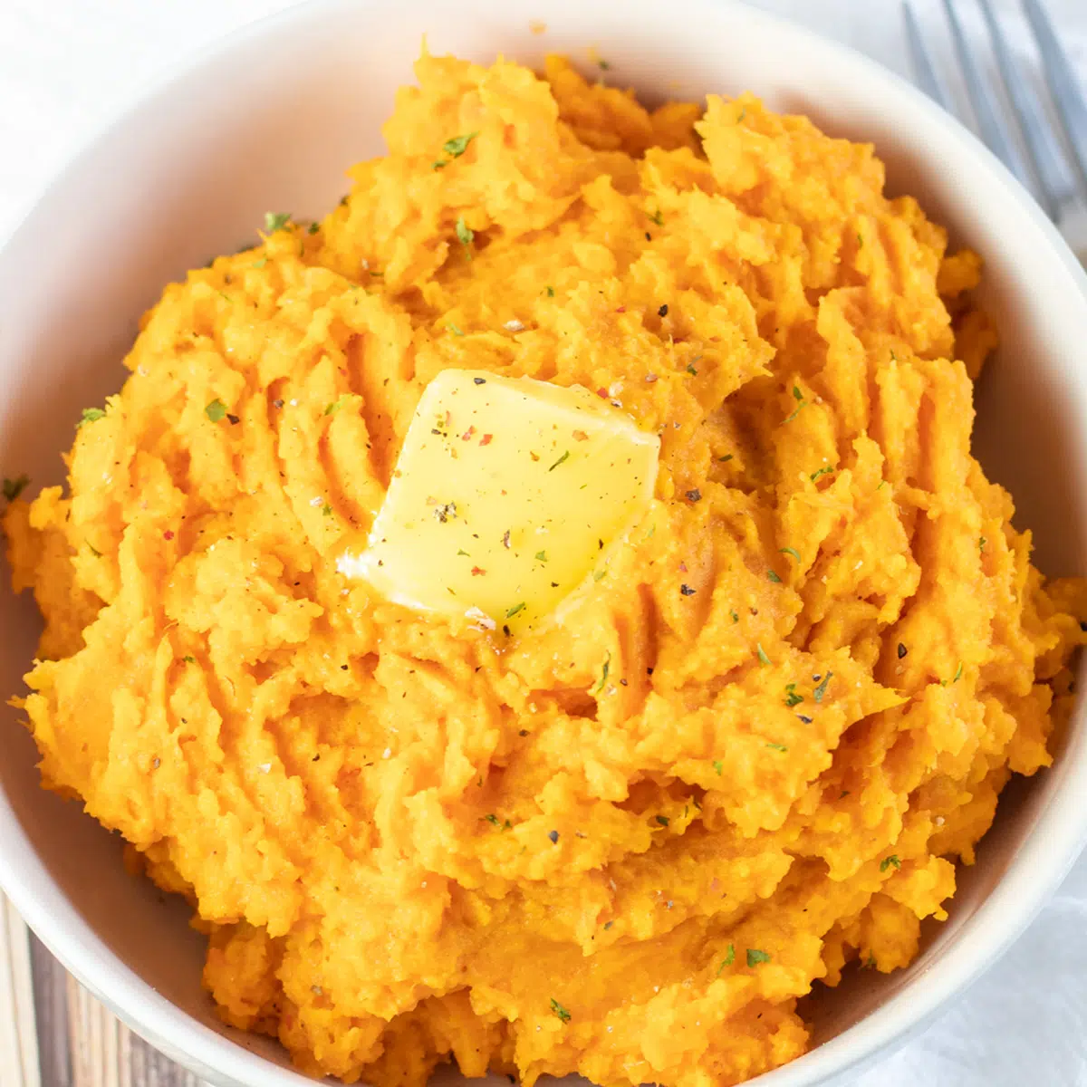 Square image of mashed sweet potatoes in a white bowl.