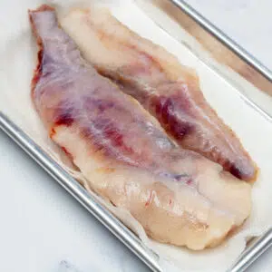 Square image of raw monkfish on a tray.