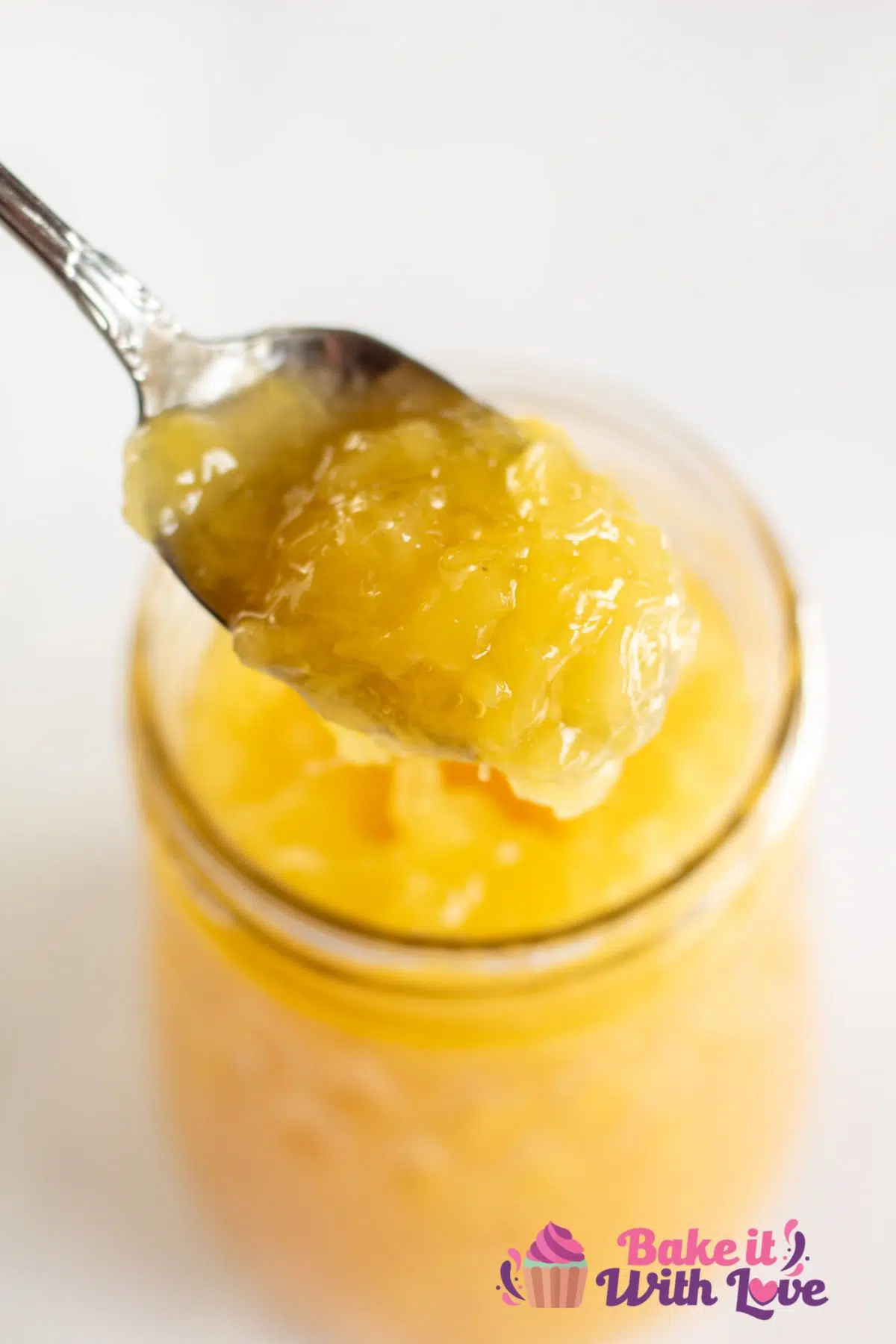 Tall image of pineapple pie filling in a glass jar with a spoonful of filling.