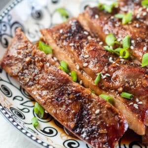Square image of roasted aisian pork belly slices covered in sesame seeds and green onion.