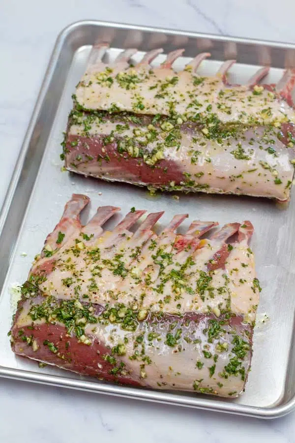 Process image 3 showing herb crusted full lamb racks on a baking sheet ready to go into the oven.