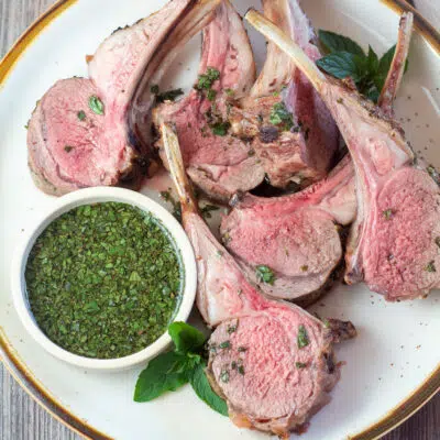 Square image of lamb chops from the rack of lamb, on a plate with mint sauce.