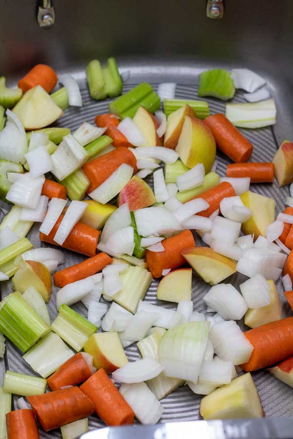 Process photo 1 showing cut up veggies and apples in the bottom of a roasting pan.