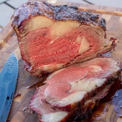 Square image of smoked bison prime rib on a wood cutting board.
