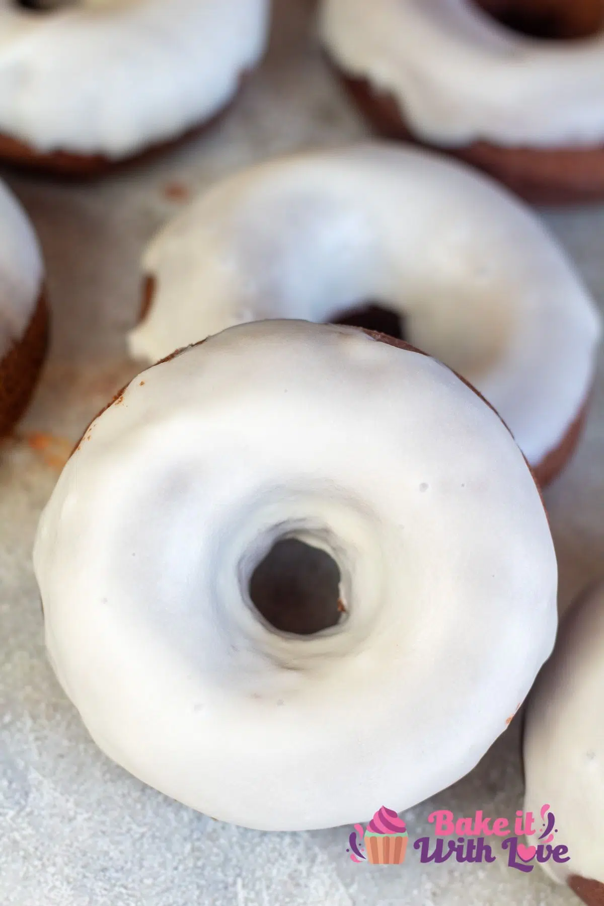 Tall image of vanilla glaze over chocolate donuts.