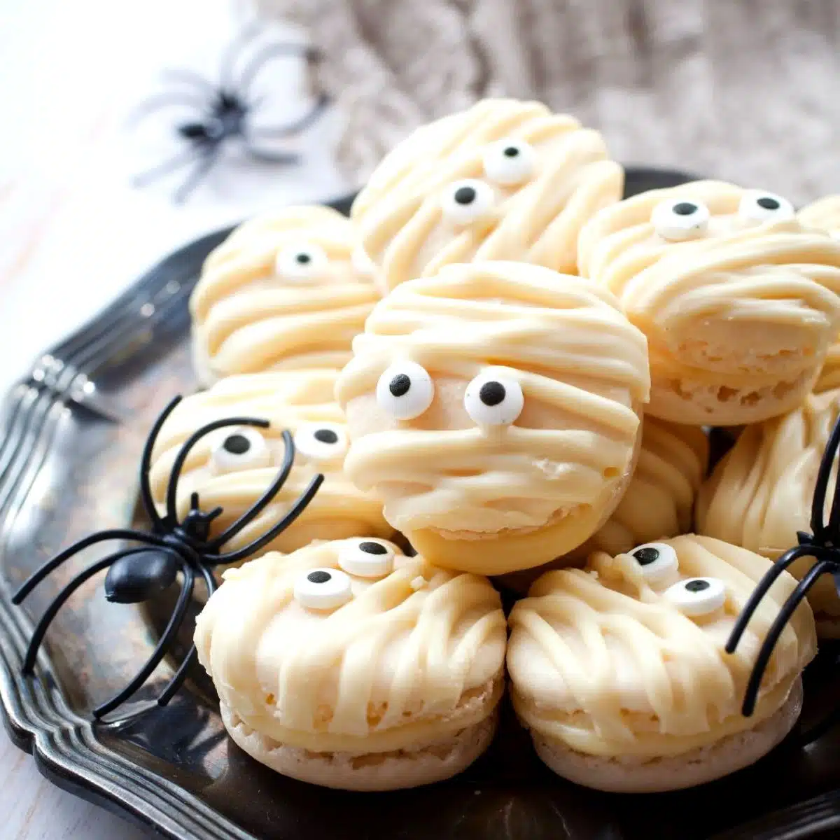 Los mejores macarons de momia en plato negro con decoración de araña de Halloween.